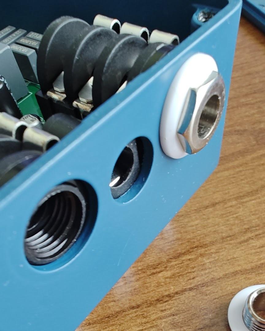 Photo of unlidded Wampler Triumph.  A Neutrik NMJ6HCD2 jack sits inside the case and the ferrule threads into the jack through the whole in the side of the case.